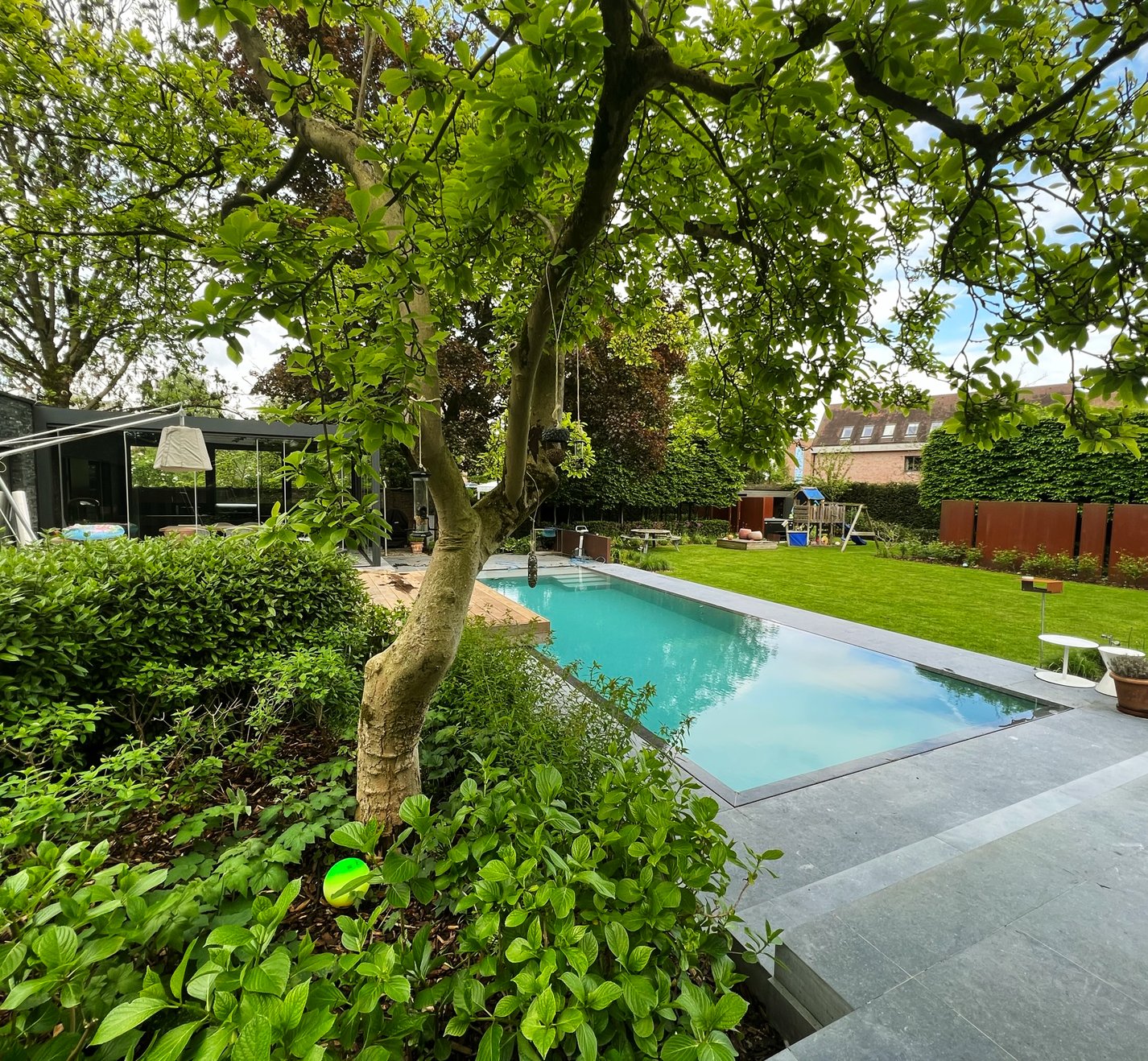 zwembad in tuin met moderne woning en speeltuin